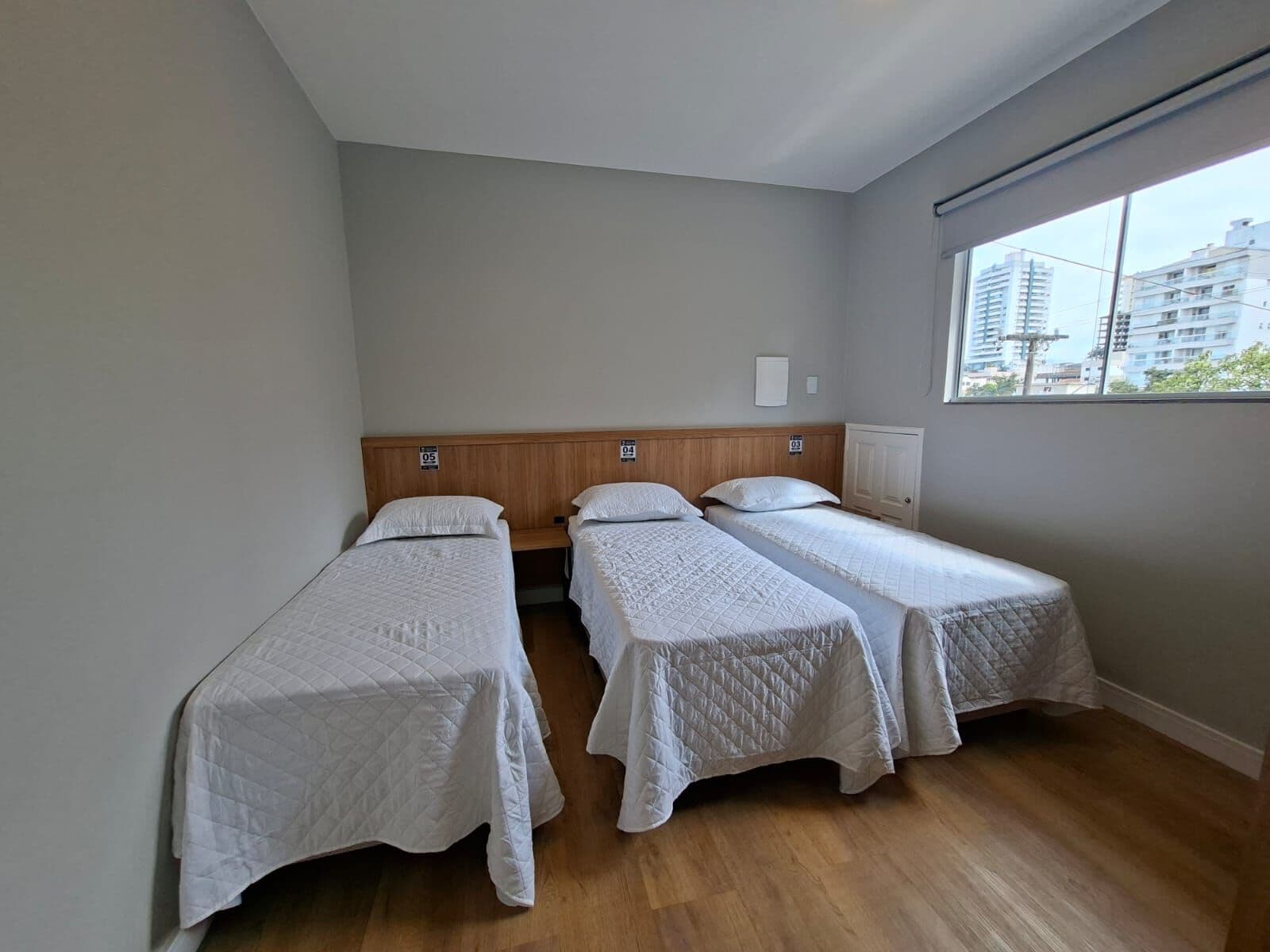 Quarto com três camas de solteiro e janela ampla