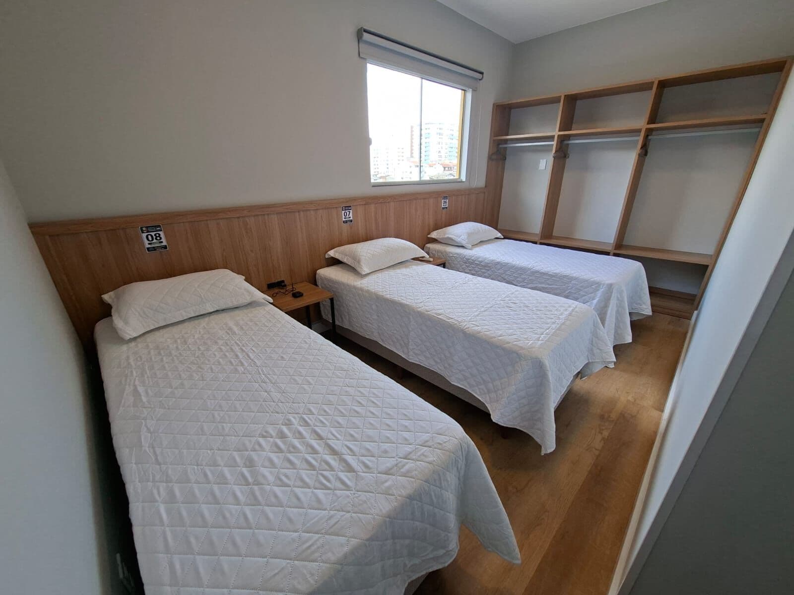 Quarto com três camas de solteiro e armário aberto